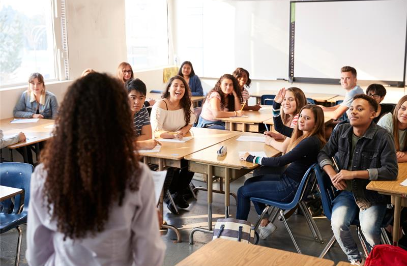 Teacher addressing classroom of children, one child raising hand