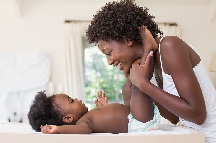 Image of woman holding baby's legs and smiling