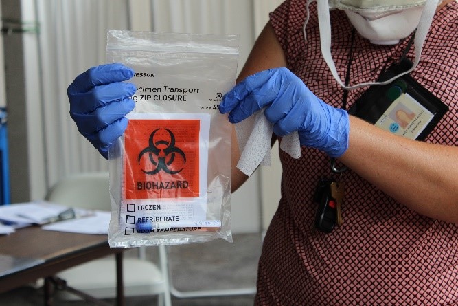 Health practitioner holding a biohazard marked bag with specimens for Covid 19 testing.