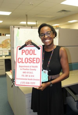 woman holding sign.  Pool closed department of health in pinellas county 64E-9 F.A.C. F.S. 381 & 514 Environmental health division (727) 538-7277